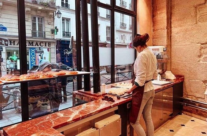 A baker at work behind a marble counter, the street visible through the tall windows