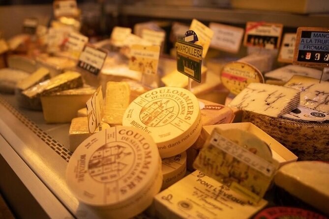 A cheesemonger's counter, rounds of Coulommiers and wedges of hard cheese under handwritten labels