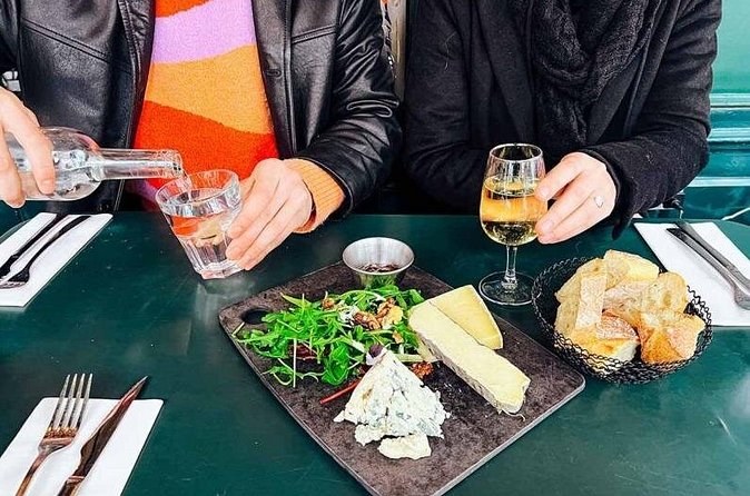 A cheese plate with salad and bread, water and white wine being poured at a café table