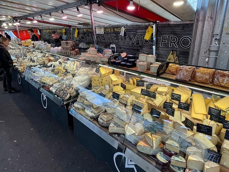 A long cheese stall at a Paris market, wedges and rounds under a striped awning