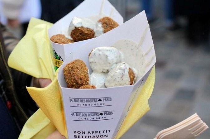 Two paper cones of falafel with tahini, the wrapping printed with a Rue des Rosiers address