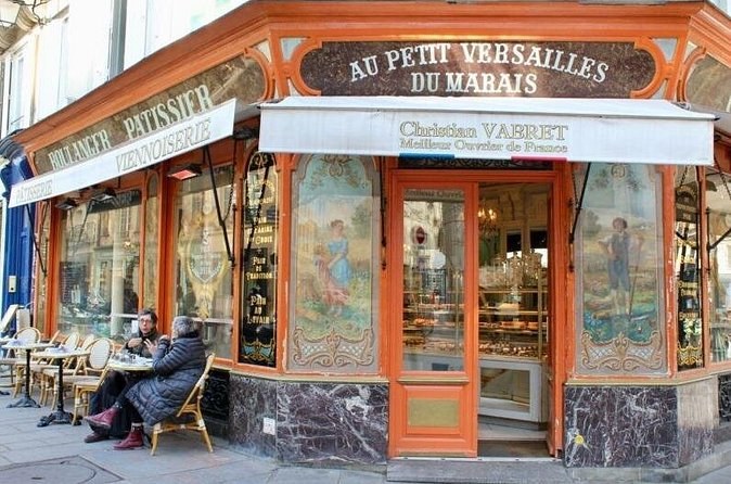 The painted corner front of a Marais boulangerie-pâtisserie, two people at a table outside