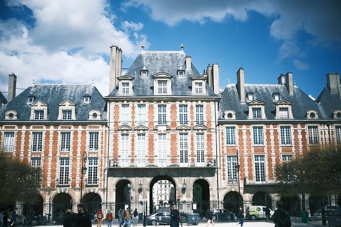 A pavilion of the Place des Vosges, red brick and pale stone under a steep slate roof, standing a story above its neighbors over the arcade
