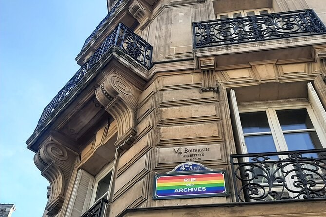 A corner townhouse with wrought-iron balconies and the Rue des Archives street sign painted in rainbow colors